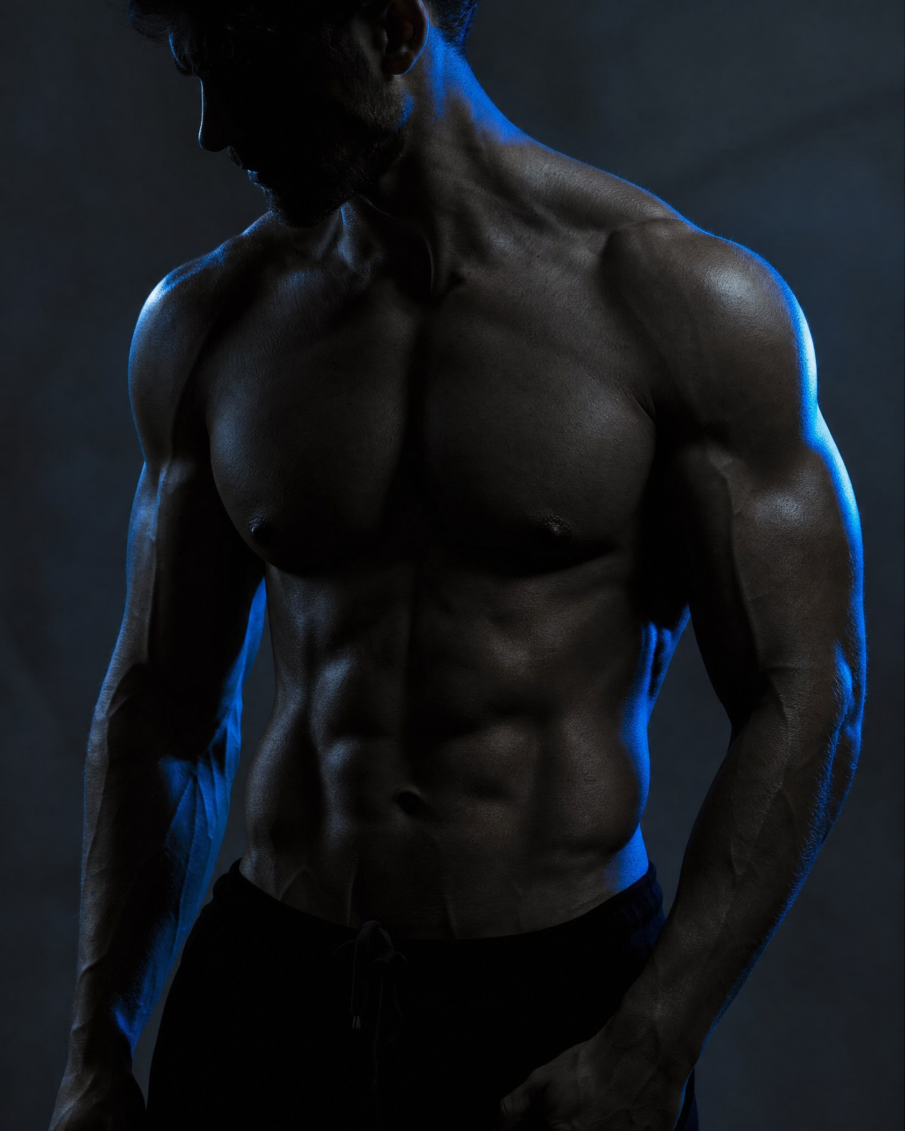 Shredded bodybuilder torso with athletic muscle definition under dramatic blue studio lighting